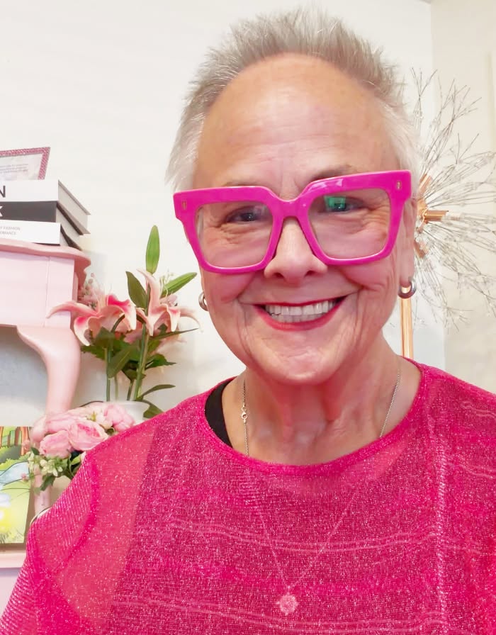 Sandy Parker Martinez smiling in bright pink glasses and a sparkling pink top